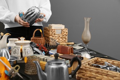 Photo of Woman holding decorative cactus above table with different stuff near grey wall, closeup. Garage sale