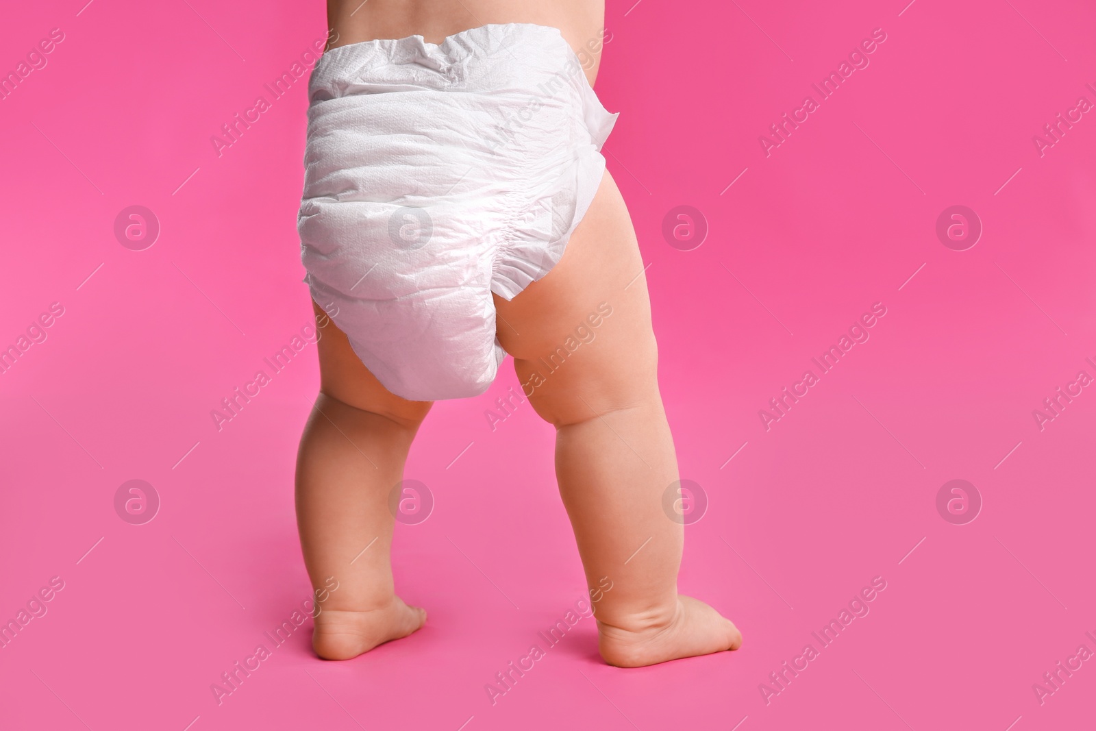 Photo of Back view of cute baby in dry soft diaper standing on pink background, closeup