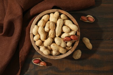 Photo of Fresh unpeeled peanuts in bowl on wooden table, top view