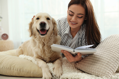 Young woman with book and her Golden Retriever at home. Adorable pet