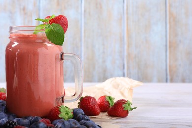 Photo of Mason jar of berry smoothie and fresh ingredients on white wooden table. Space for text