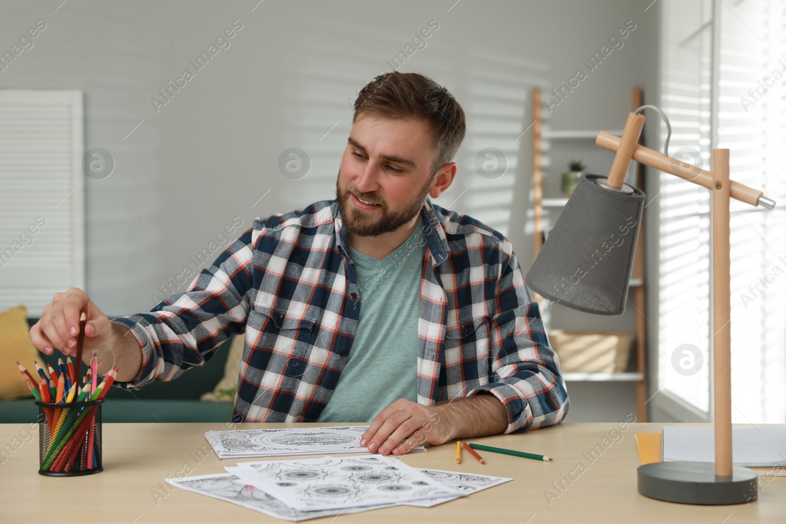 Photo of Young man coloring antistress picture at table indoors