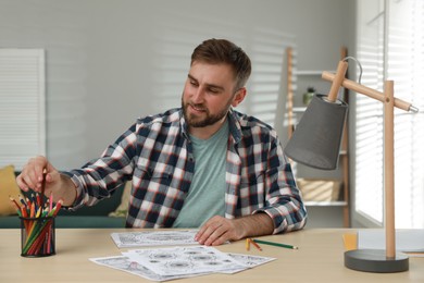 Young man coloring antistress picture at table indoors