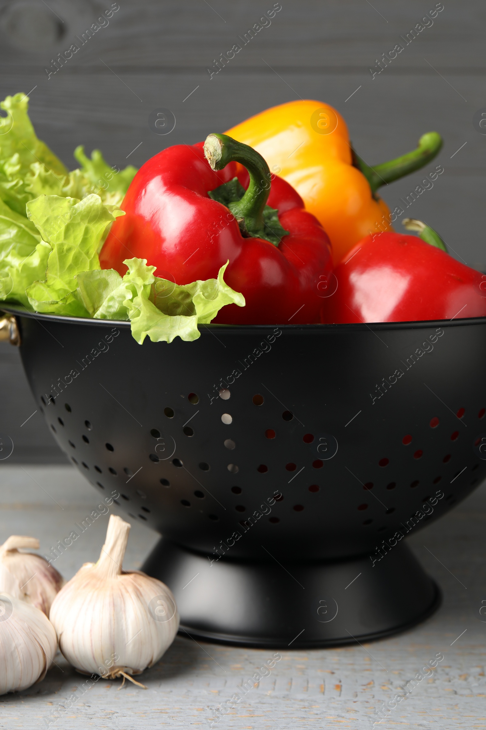 Photo of Black colander and different vegetables on rustic wooden table, closeup