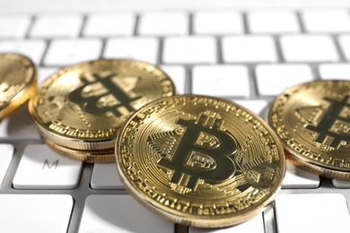 Golden bitcoins on white computer keyboard, closeup view