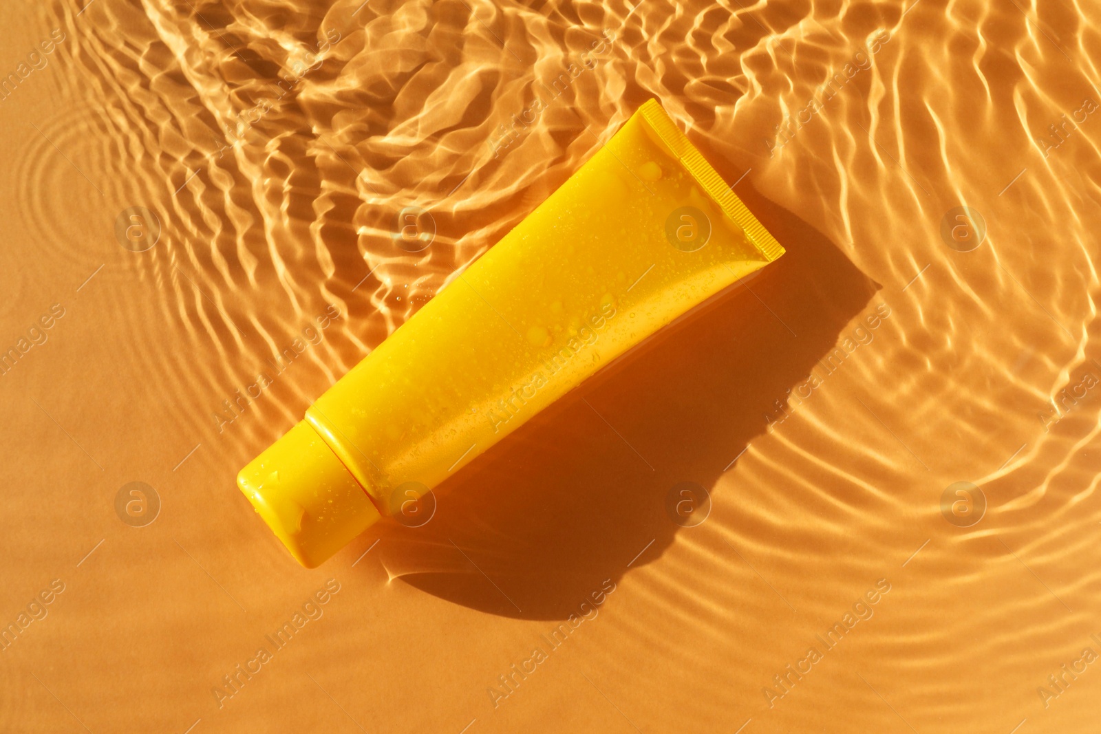 Photo of Tube with moisturizing cream in water on orange background, top view