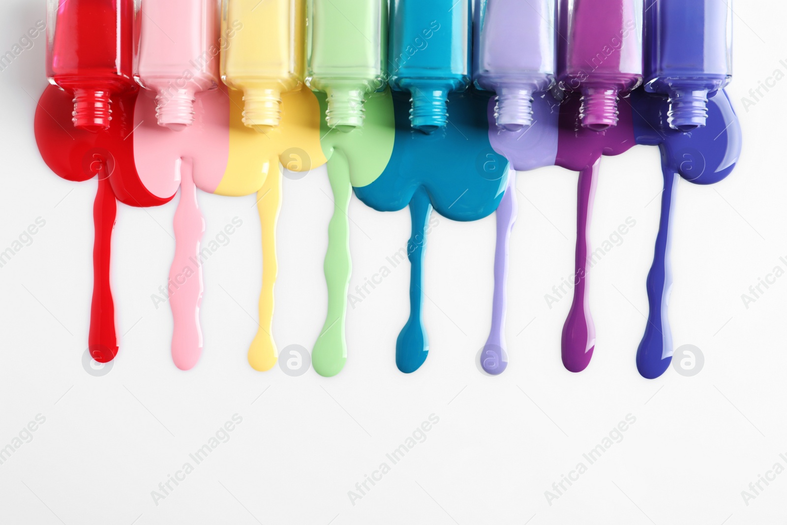 Photo of Spilled colorful nail polishes and bottles on white background, top view