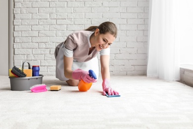 Photo of Chambermaid woman cleaning carpet indoors
