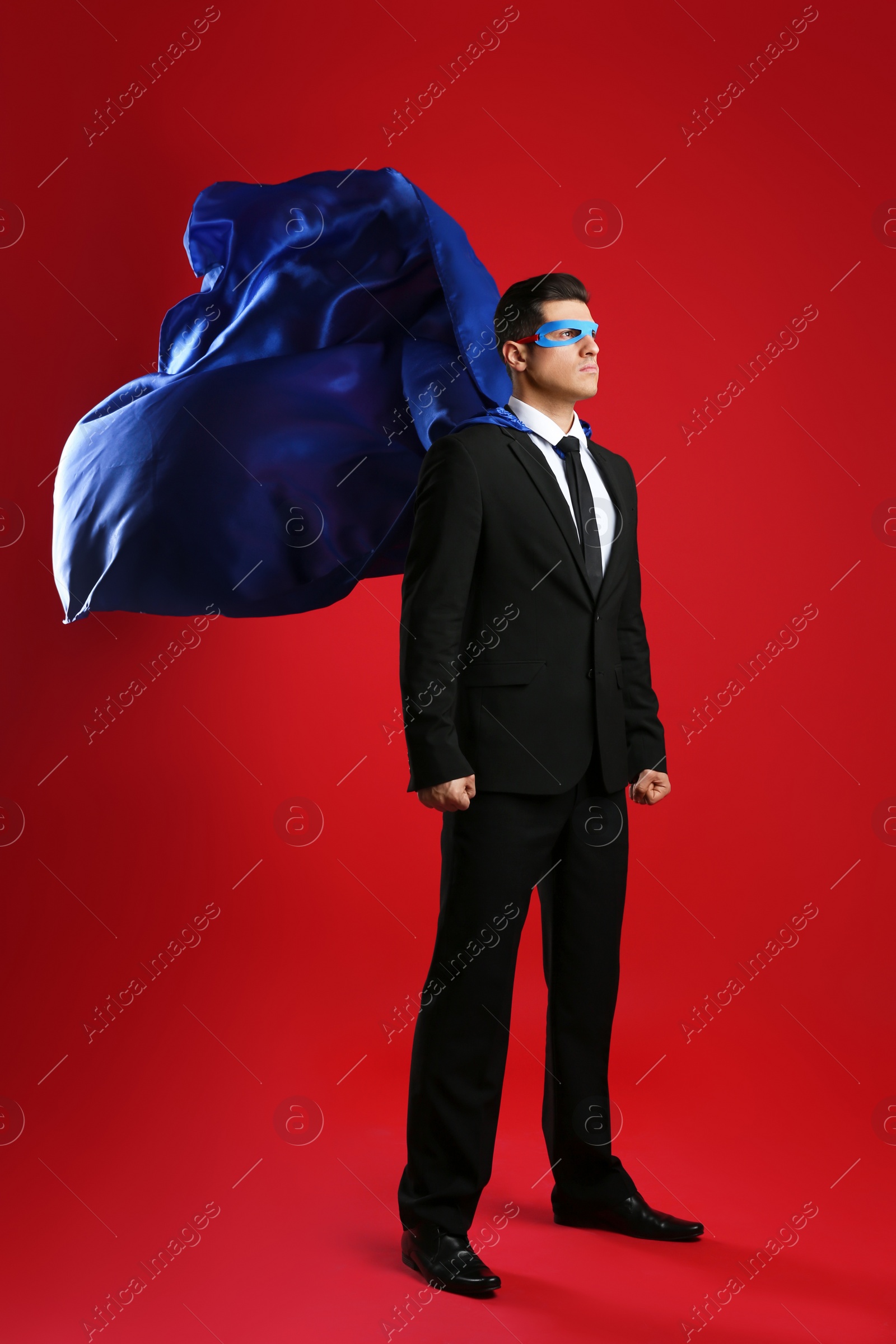 Photo of Businessman wearing superhero cape and mask on red background