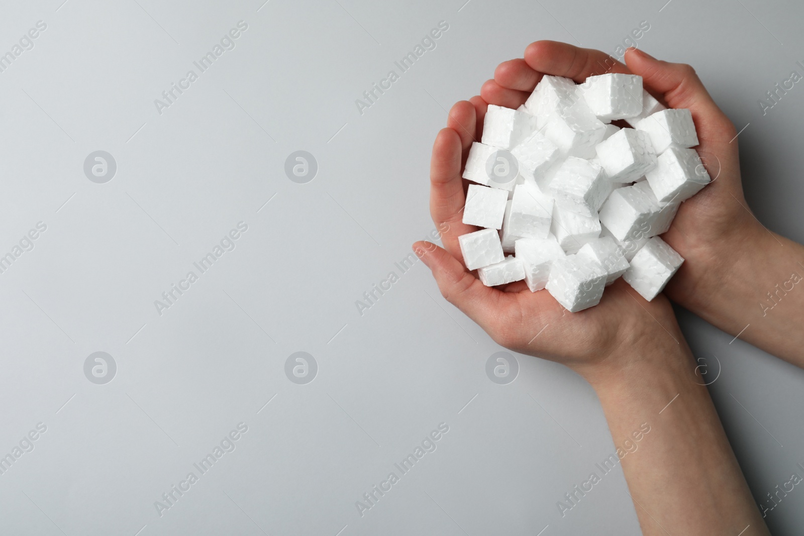 Photo of Woman with handful of styrofoam cubes on light grey background, top view. Space for text