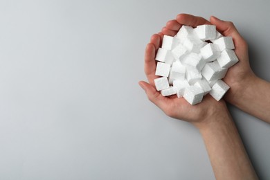 Woman with handful of styrofoam cubes on light grey background, top view. Space for text