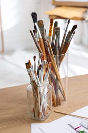 Photo of Holders with different paintbrushes on wooden table indoors. Artist's workplace
