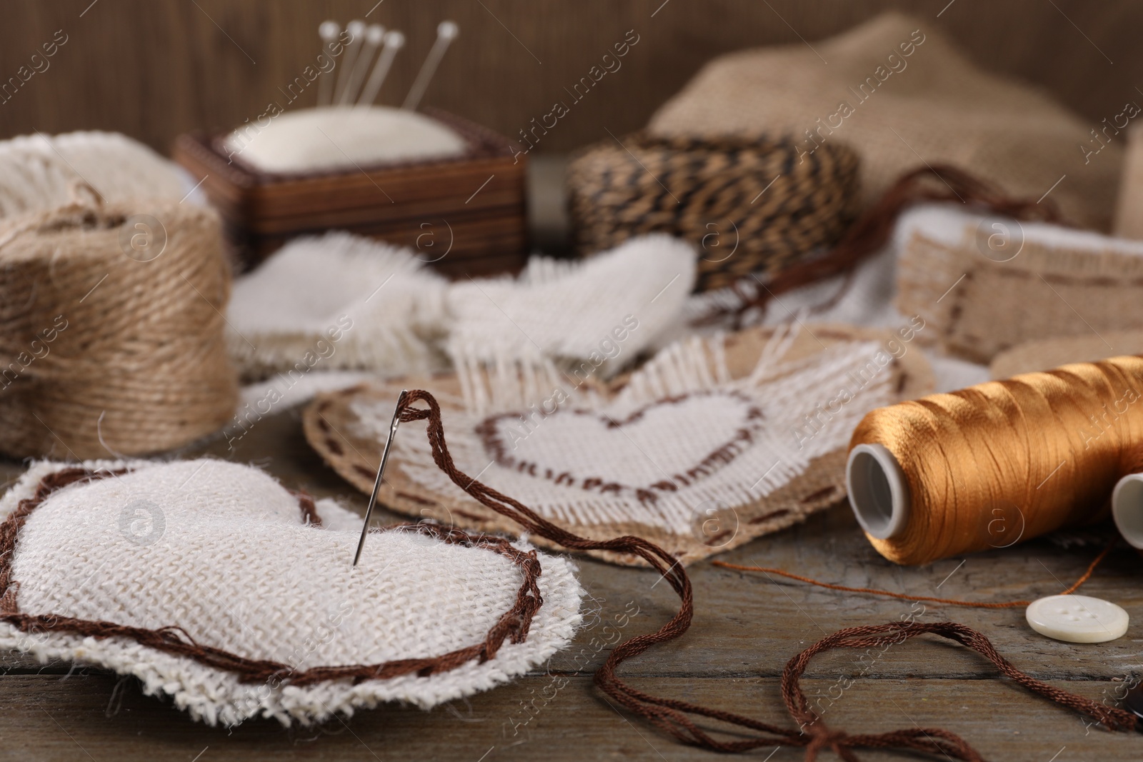 Photo of Pieces of burlap fabric with different stitches and needle with thread on wooden table, closeup