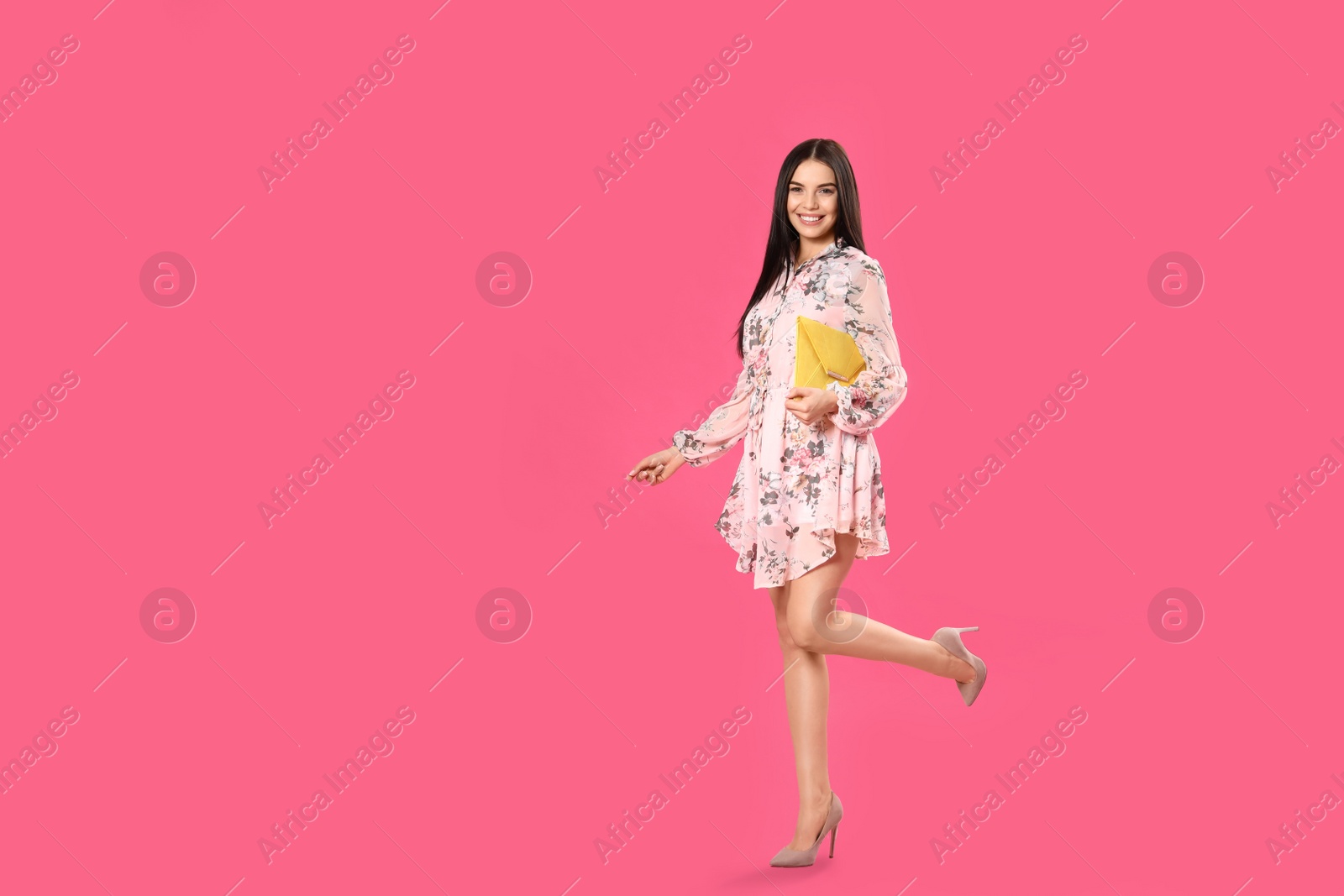 Photo of Young woman wearing floral print dress with elegant clutch on pink background