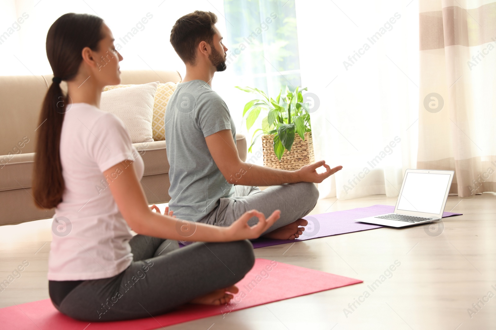 Photo of Couple practicing yoga while watching online class at home during coronavirus pandemic. Social distancing