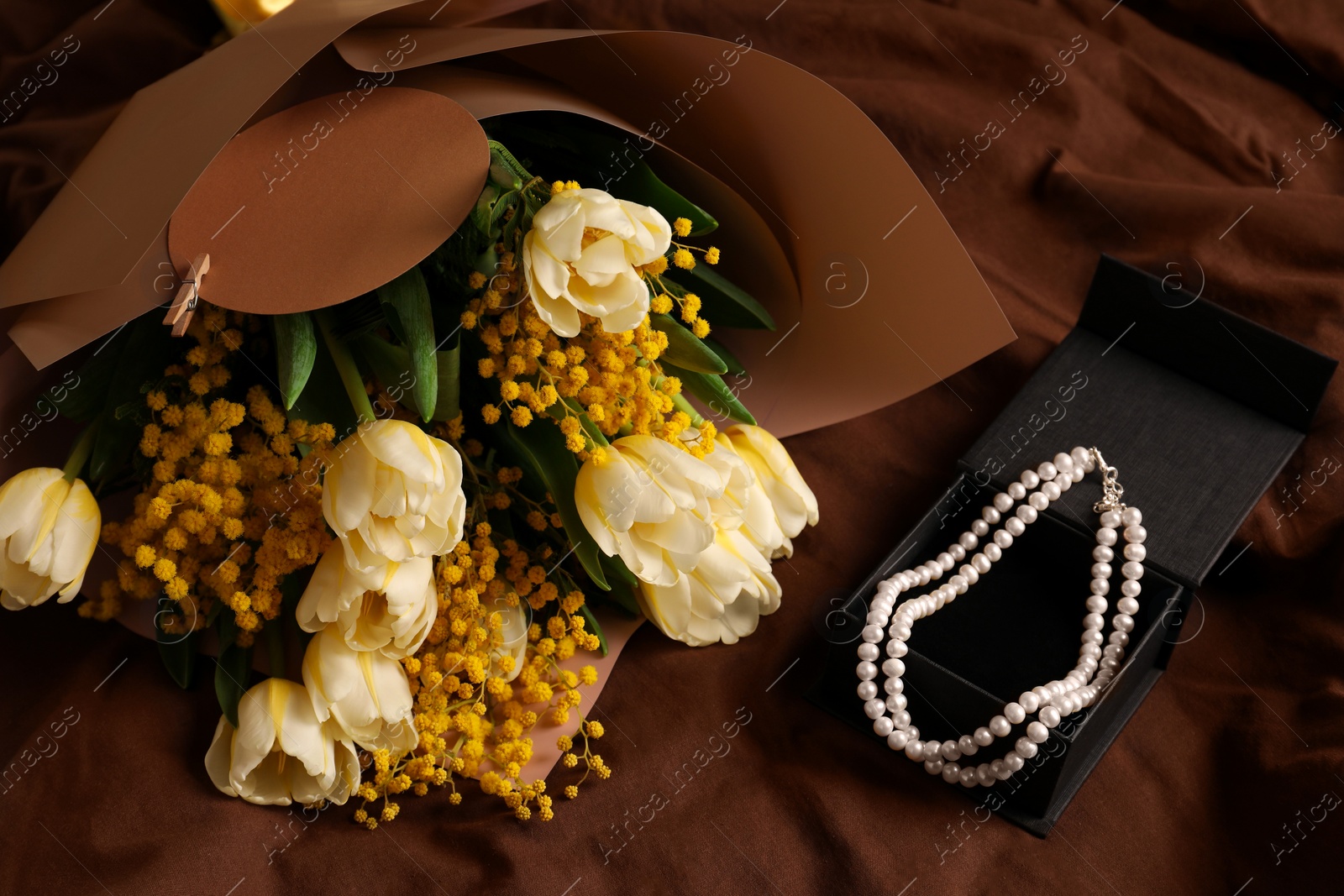 Photo of Bouquet of beautiful spring flowers and necklace on brown fabric, above view