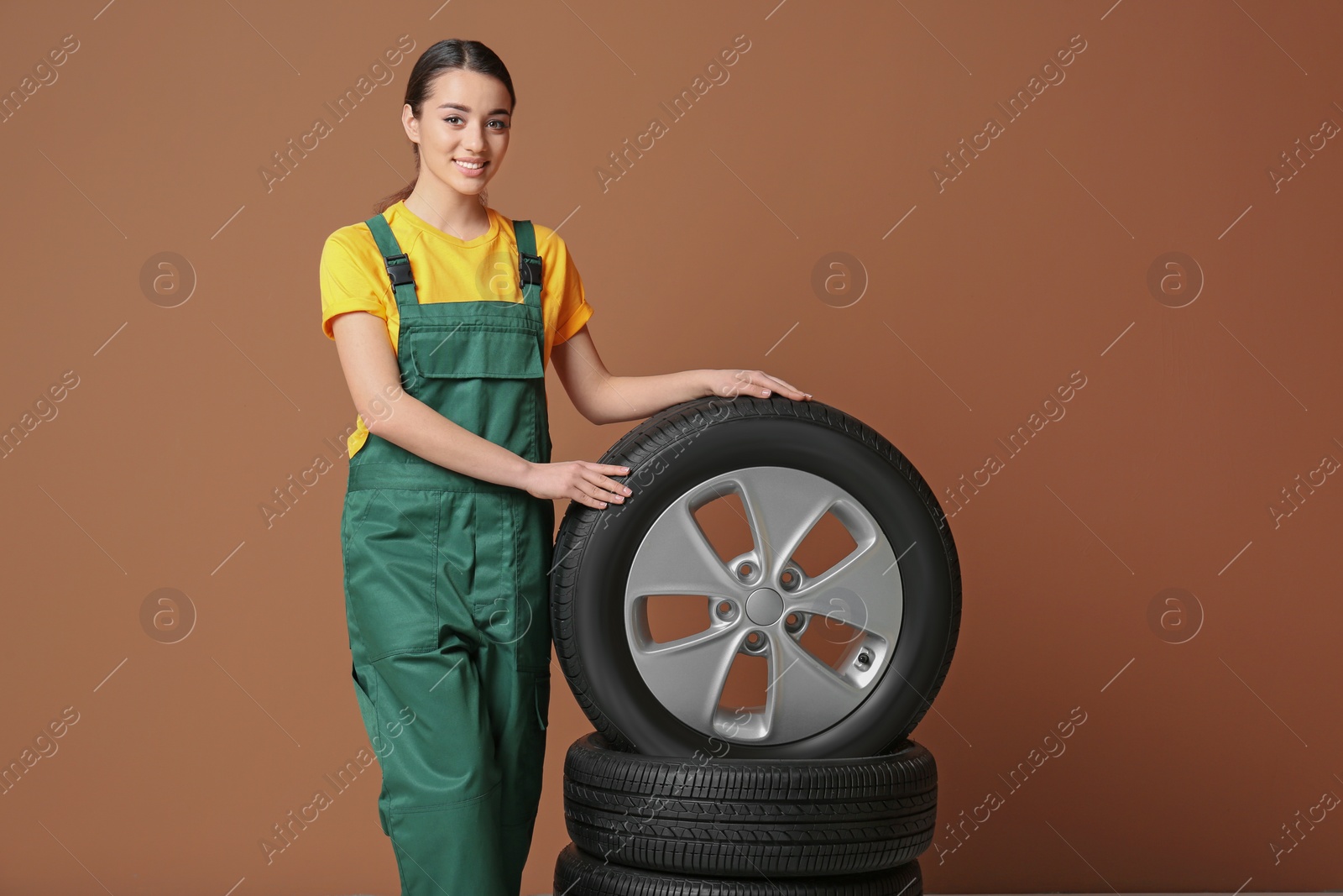 Photo of Female mechanic in uniform with car tires on color background