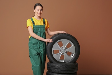 Female mechanic in uniform with car tires on color background