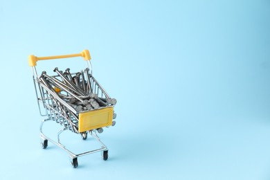 Metal nails in shopping cart on light blue background, space for text