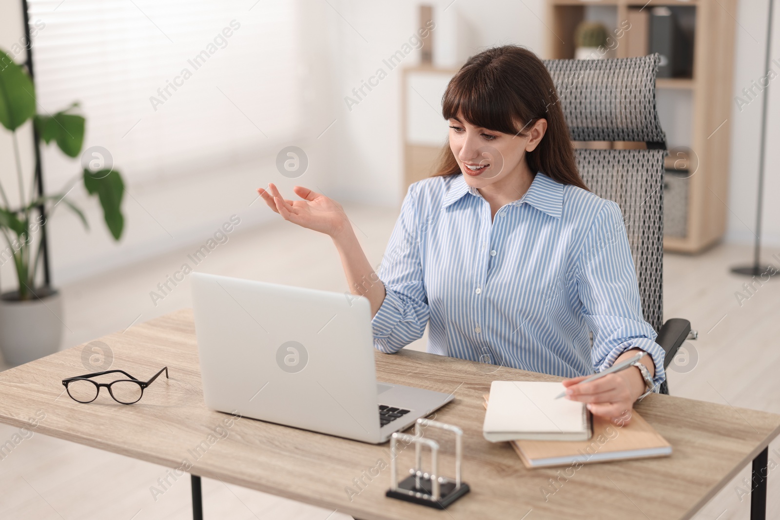 Photo of Woman taking notes during webinar at wooden table indoors