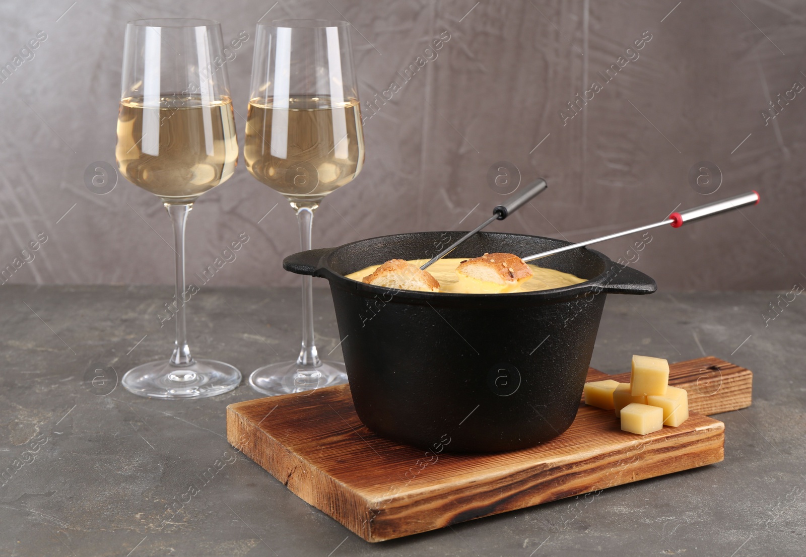Photo of Fondue pot with tasty melted cheese, forks, bread and wine on grey table