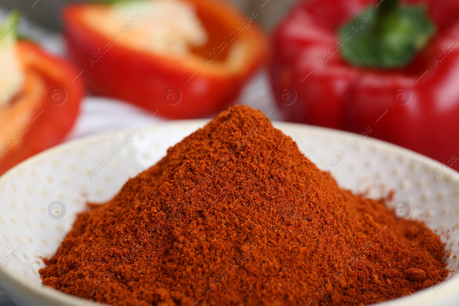 Photo of Bowl with aromatic paprika powder near fresh bell peppers, closeup