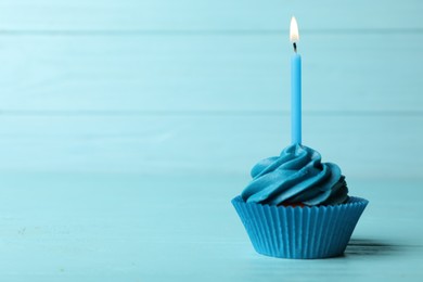 Delicious birthday cupcake with cream and burning candle on blue wooden background. Space for text