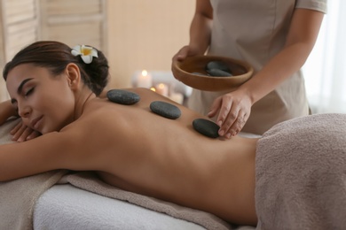 Beautiful young woman getting hot stone massage in spa salon