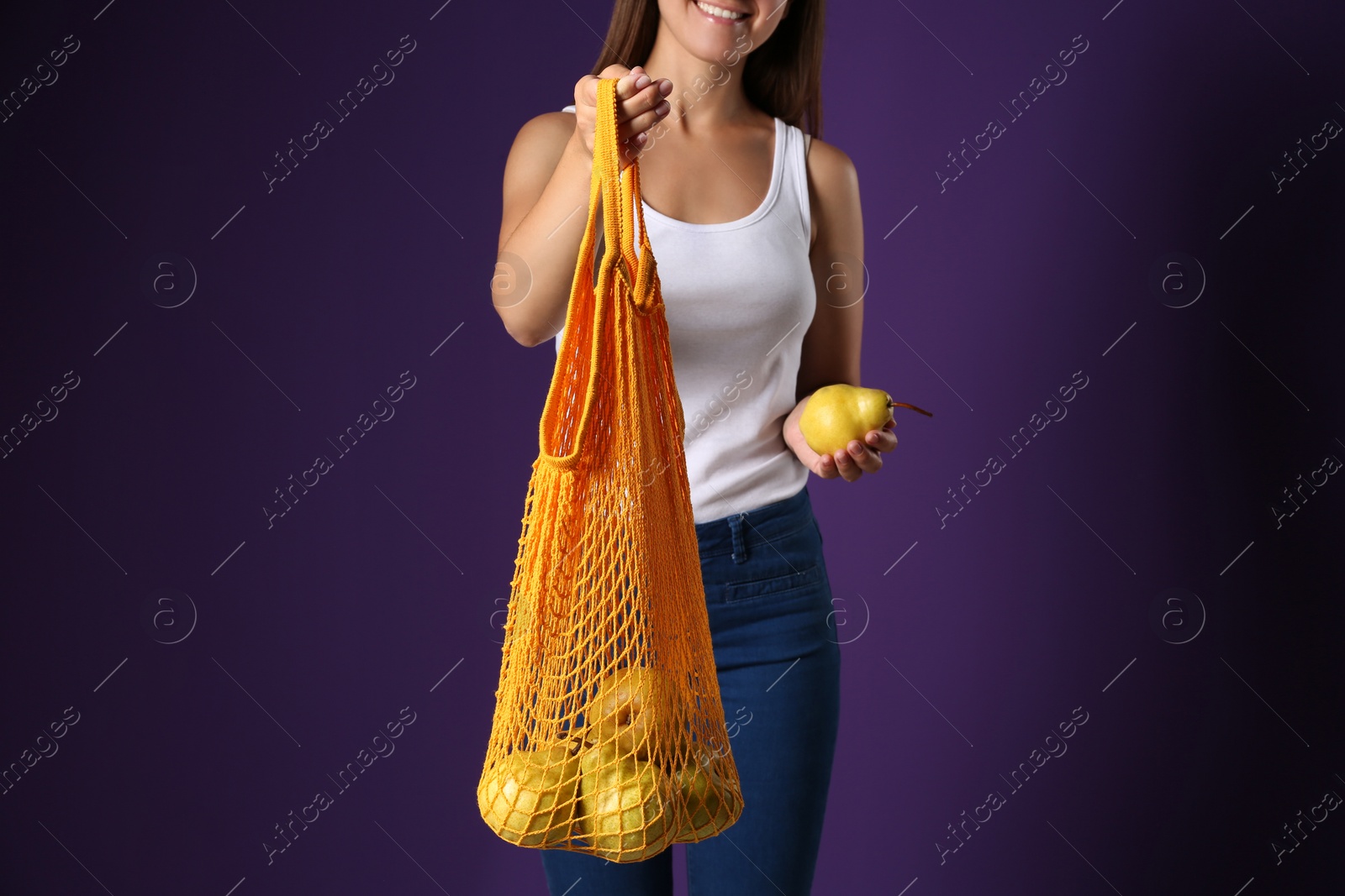 Photo of Woman holding net bag with fresh ripe pears on purple background, closeup