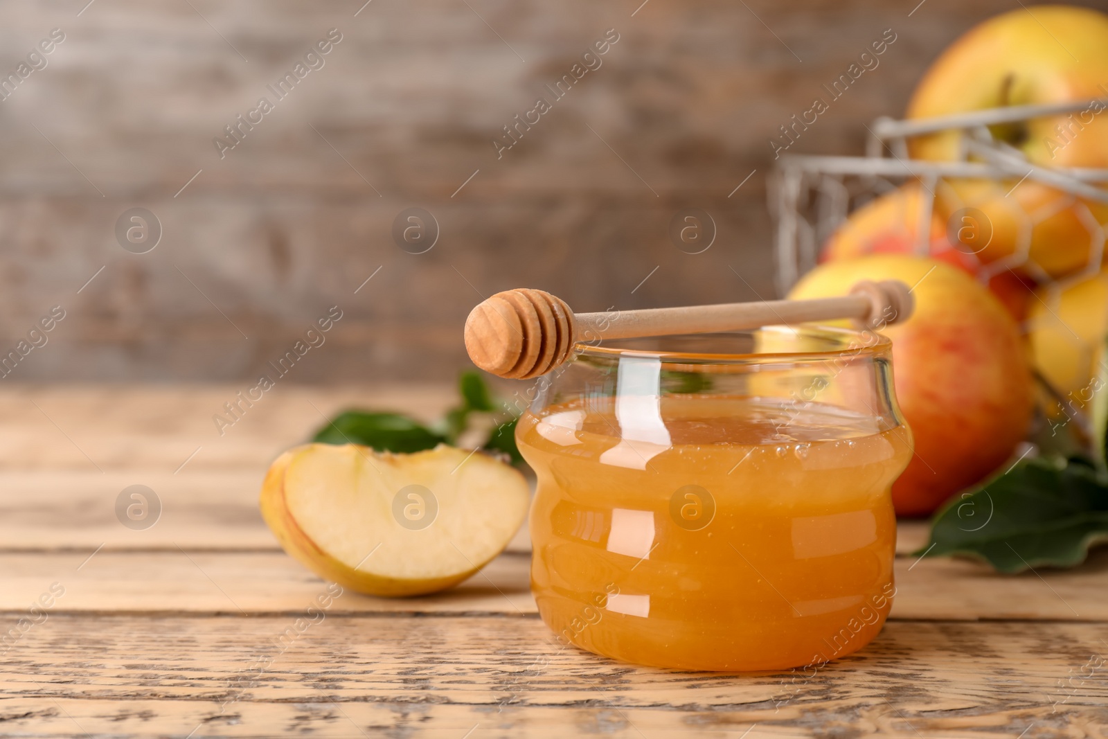 Photo of Jar of honey, dipper and apples on wooden table