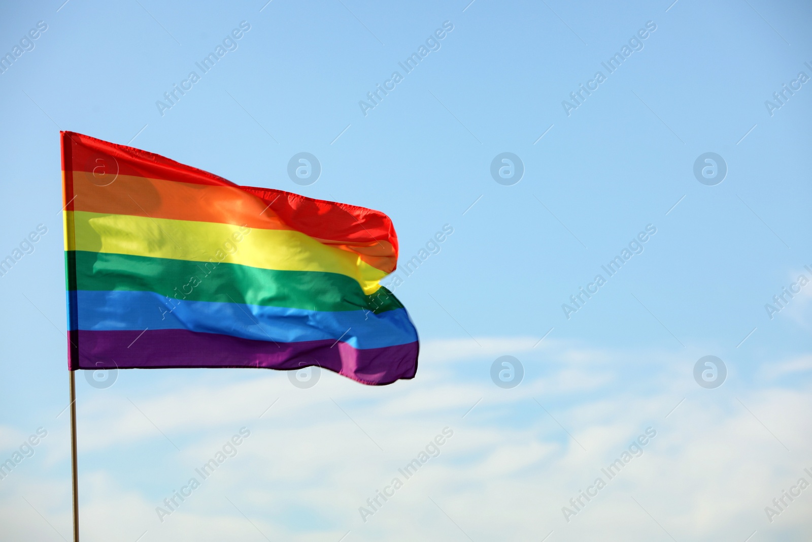 Photo of Bright LGBT flag against blue sky with clouds, space for text