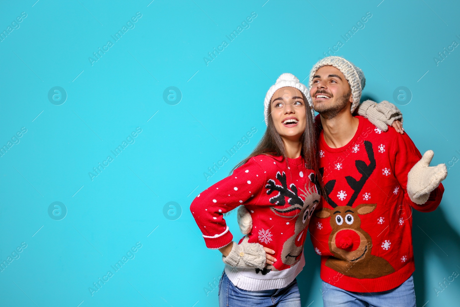 Photo of Young couple in Christmas sweaters and knitted hats on color background. Space for text
