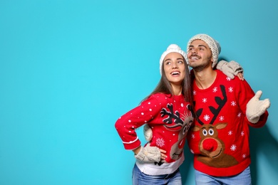 Photo of Young couple in Christmas sweaters and knitted hats on color background. Space for text