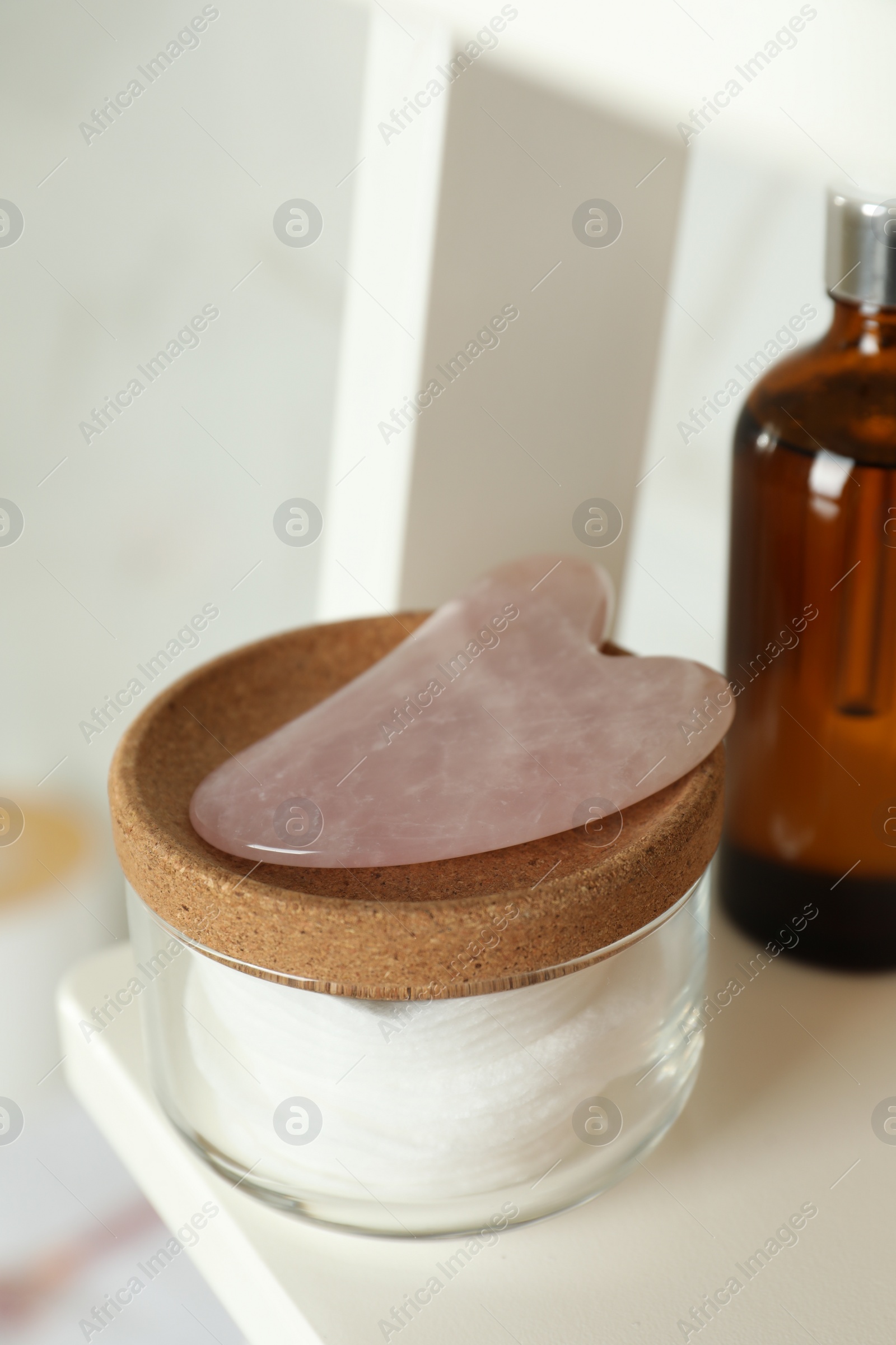 Photo of Rose quartz gua sha tool and toiletries on white shelf