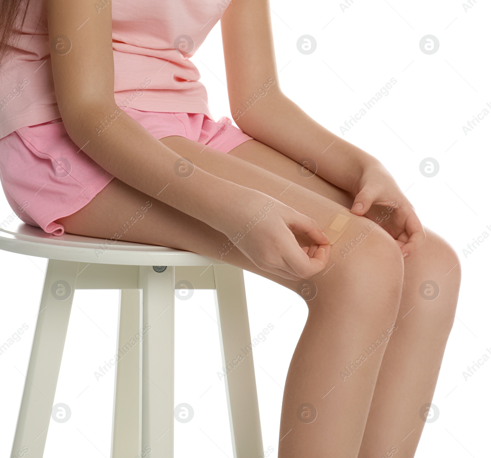 Photo of Girl putting sticking plaster onto leg on white background, closeup