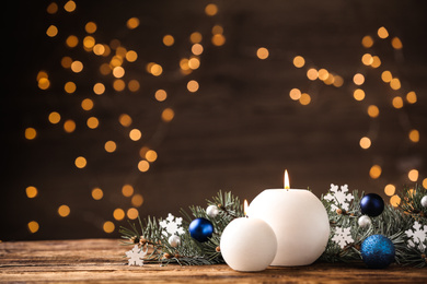 Candles and Christmas decor on wooden table against blurred festive lights, space for text. Winter holiday