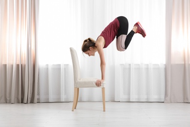 Photo of Young woman exercising with chair indoors. Home fitness