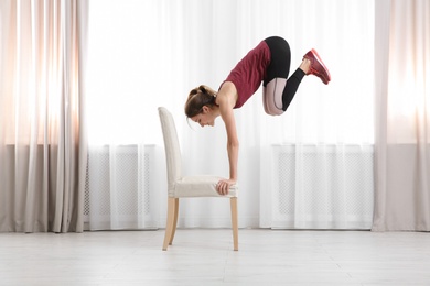 Young woman exercising with chair indoors. Home fitness