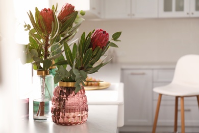 Photo of Beautiful protea flowers on countertop in kitchen, space for text. Interior design