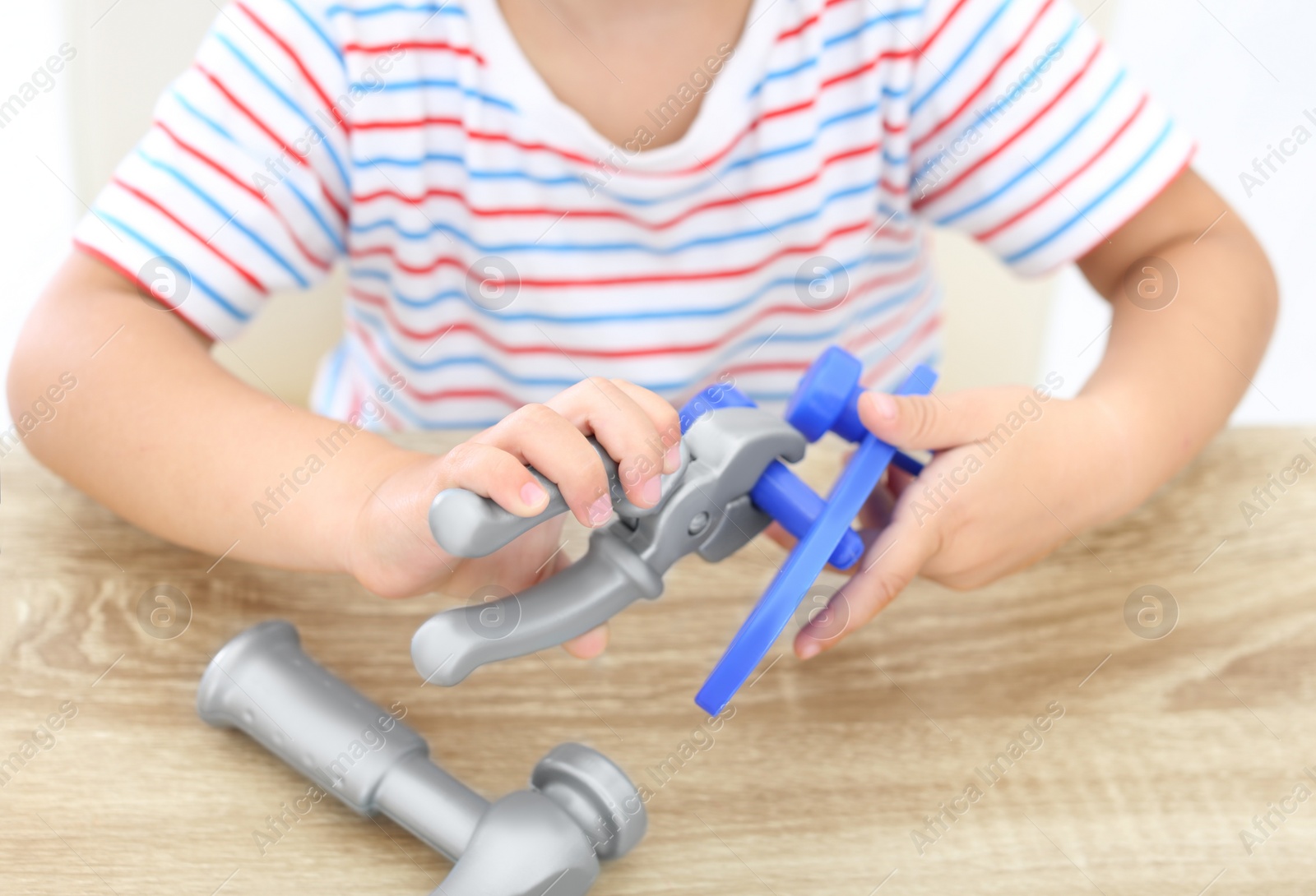 Photo of Little boy playing with toy construction tools at wooden table, closeup