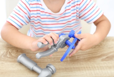 Little boy playing with toy construction tools at wooden table, closeup