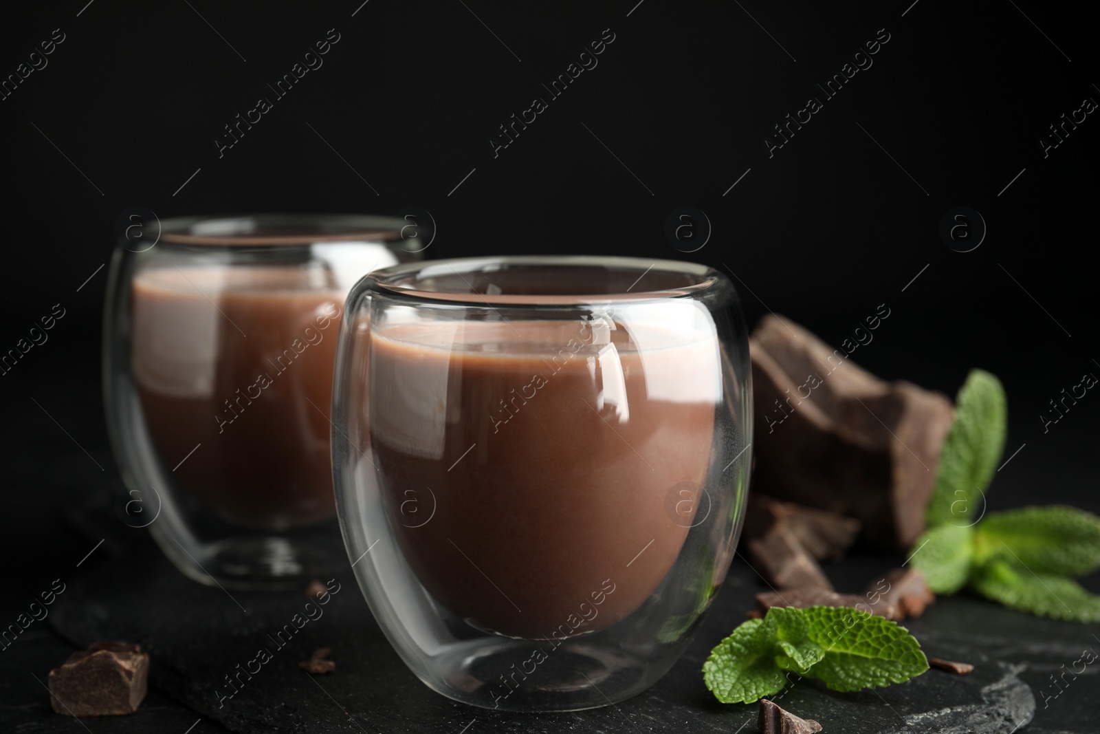 Photo of Glasses of delicious hot chocolate, chunks and fresh mint on black table