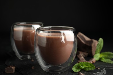 Glasses of delicious hot chocolate, chunks and fresh mint on black table
