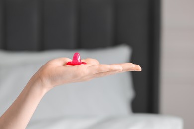 Woman holding unpacked condom on blurred background, closeup. Safe sex