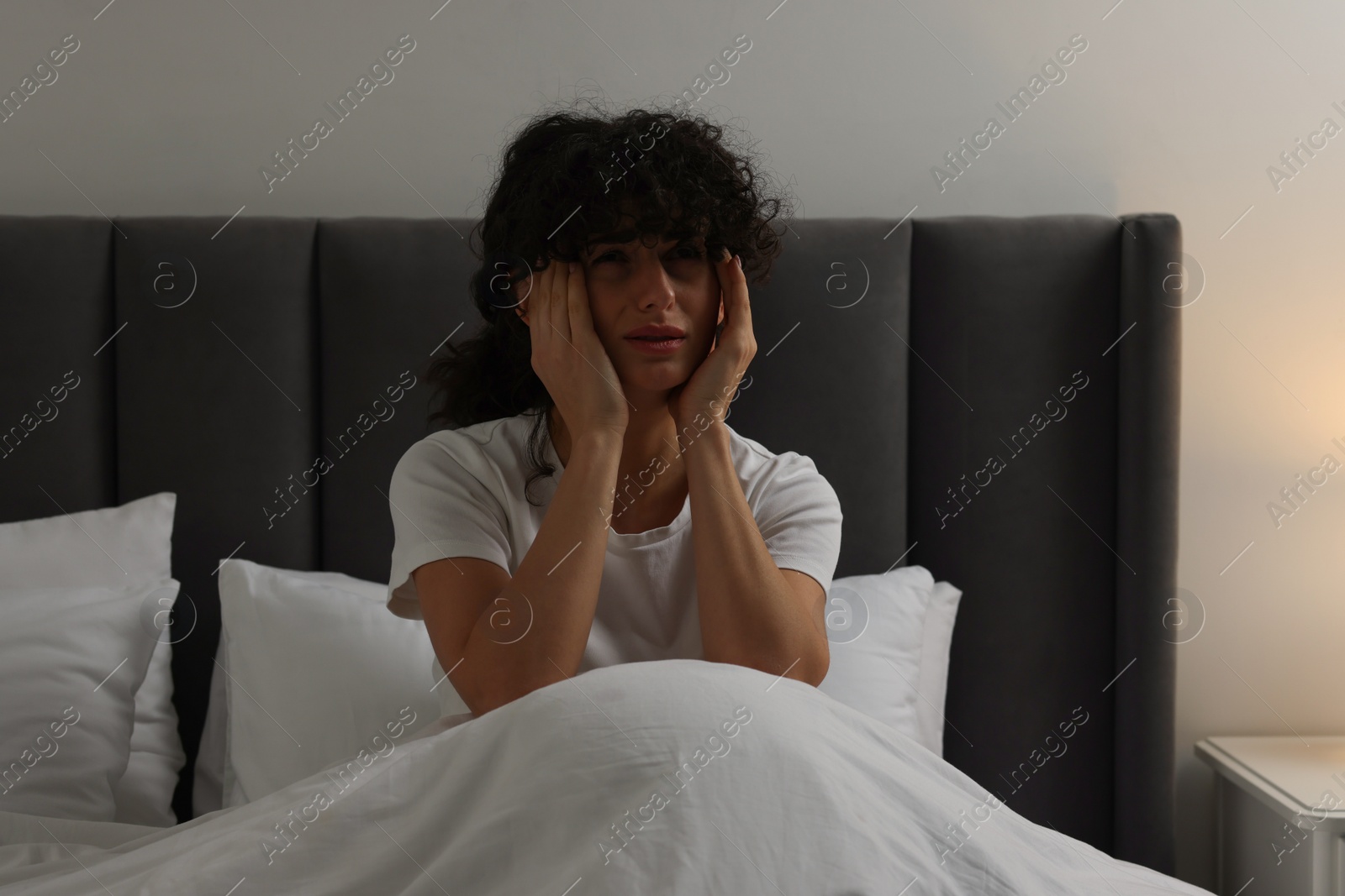 Photo of Young woman suffering from headache in bed at night