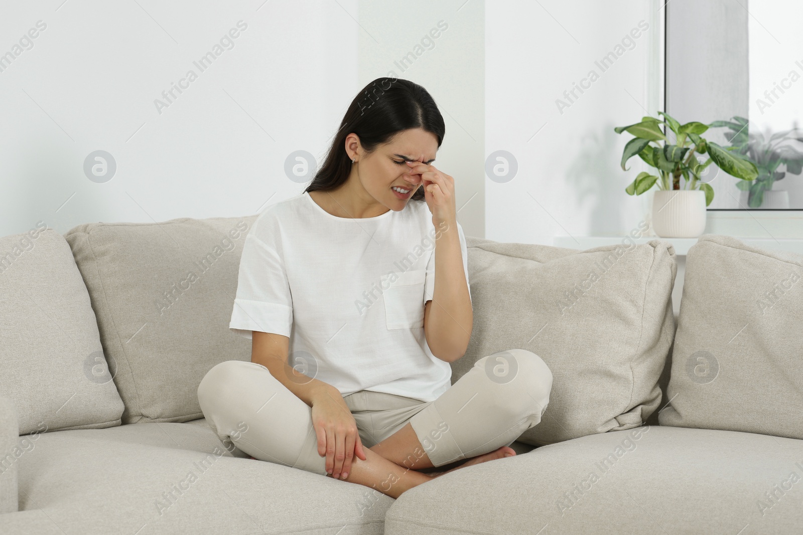 Photo of Young woman suffering from headache on sofa at home. Hormonal disorders