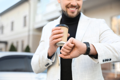 Photo of Businessman with cup of coffee on city street in morning, closeup