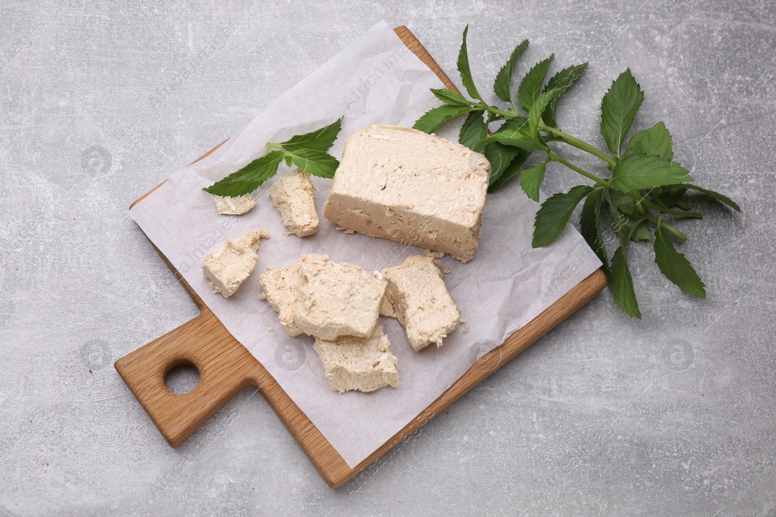 Photo of Pieces of tasty halva and mint leaves on light grey table, top view