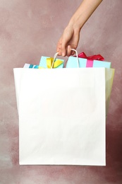 Photo of Woman holding paper shopping bag with gifts on color background