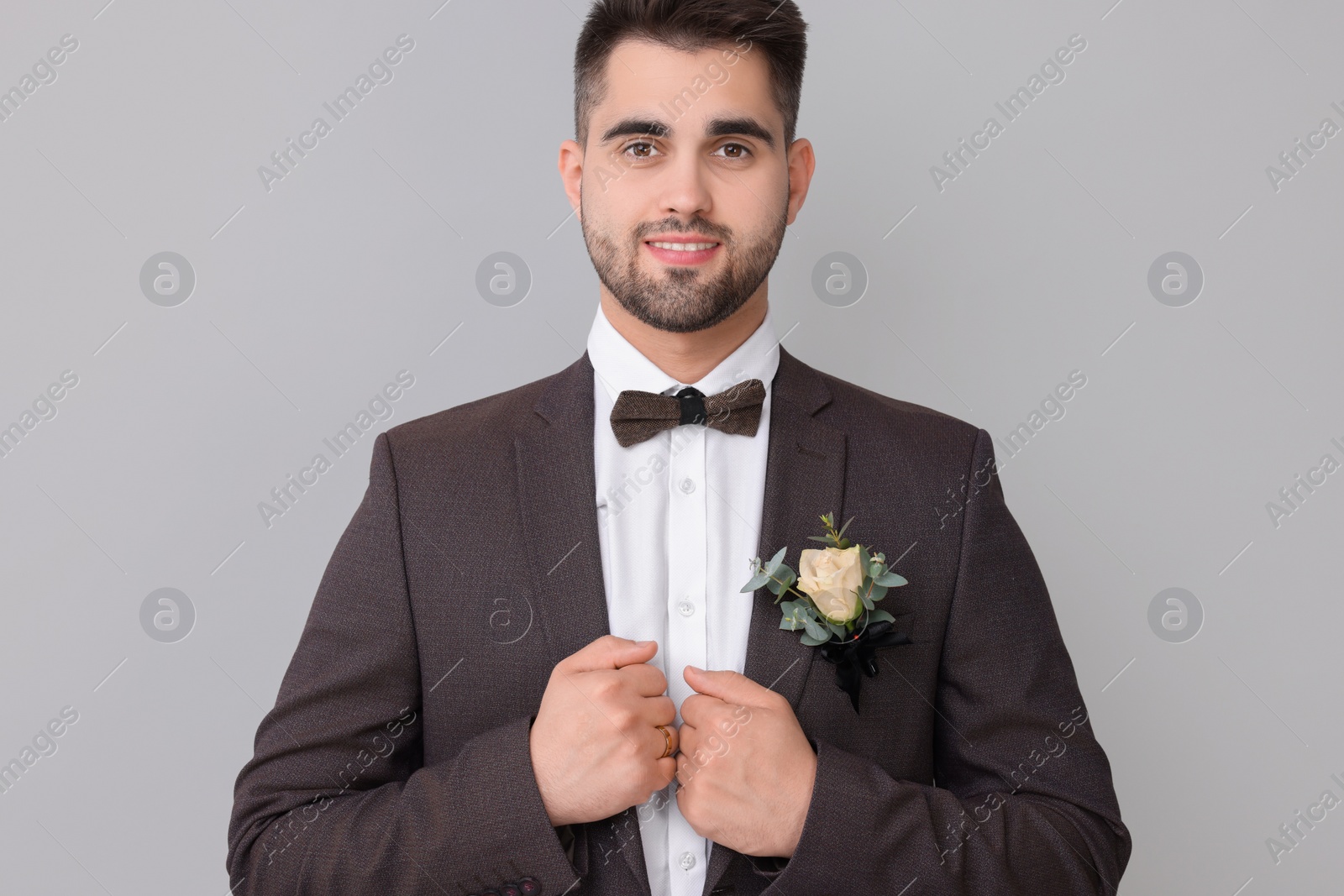 Photo of Handsome young groom with boutonniere on light grey background. Wedding accessory